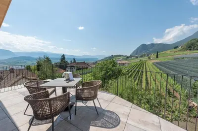 a patio with a table and chairs and a view of a vineyard at Villa Montis Exclusive Holiday Apartments in Eppan with Spectacular Views of Dolomites and Bolzano Area in Appiano sulla Strada del Vino