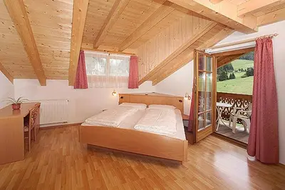 a bedroom with a bed and a table and a window at Tinahof in Selva di Val Gardena