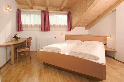 a bedroom with a bed and a desk and a window at Tinahof in Selva di Val Gardena