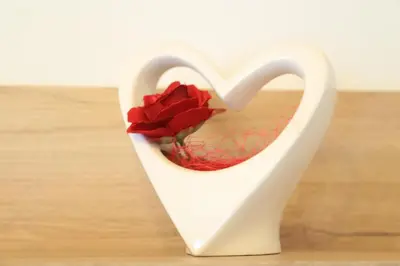 a white heart shaped vase with a red flower in it at Ferienhof Weingenuss in Cortina Sulla Strada Del Vino
