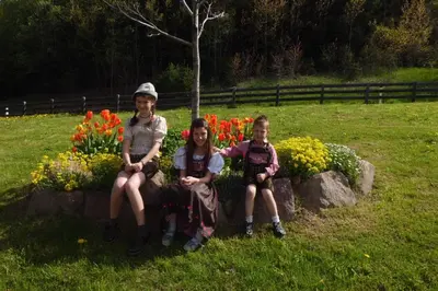 three girls sitting on a rock in front of flowers at Gasserhof Chalets in Meltina