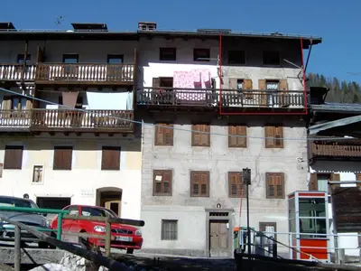 a building with balconies and a red truck parked in front of it at COL DE RIF Piccolo Appartamento Storico Dolomiti in Falcade