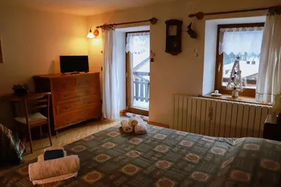 a bedroom with a bed and a dresser and a window at COL DE RIF Piccolo Appartamento Storico Dolomiti in Falcade