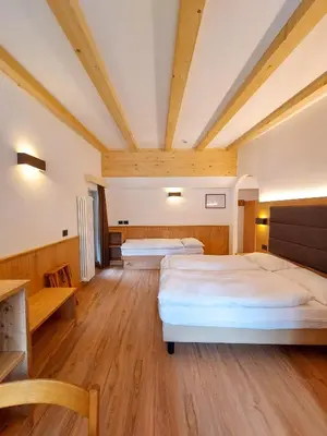 two beds in a large room with wooden floors at Appartamenti Arnica in Alba di Canazei
