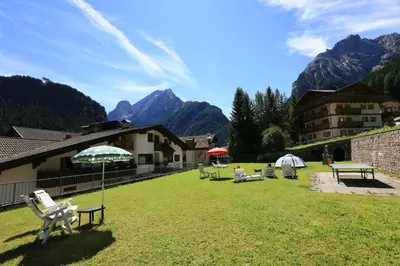 a group of chairs and umbrellas in a yard with mountains at Appartamenti Arnica in Alba di Canazei