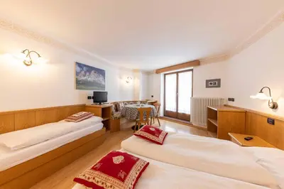 a hotel room with two beds and a table at Appartamenti Arnica in Alba di Canazei