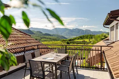a table and chairs on a balcony with a view of mountains at Prälatenhof Wine & Apartments in Caldaro