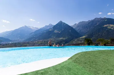 a group of people sitting in a swimming pool with mountains at Hammele Appartements in Schenna