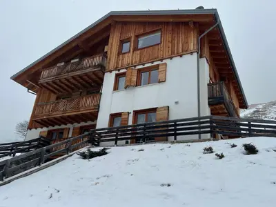 a large wooden house on top of a snow covered slope at Sunny Arabba Apartment in Arabba