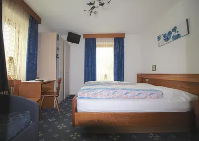 a bedroom with a bed and a desk and a window at Garní Emma in Arabba