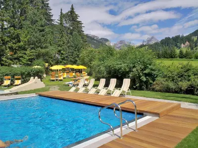 a swimming pool with chairs and a wooden deck at Residence Comploj in Santa Cristina in Val Gardena