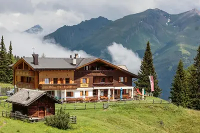 a large wooden house on a hill with mountains at Gasthaus Furlhütte in Vipiteno