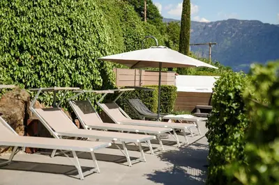 a row of white lounge chairs and an umbrella at Paloria Apartments & Sport in Lagundo