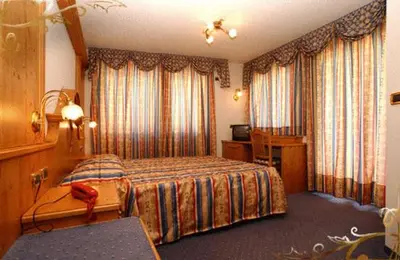 a bedroom with a bed and a desk and curtains at Family & Wellness Hotel Fontana in Vigo di Fassa