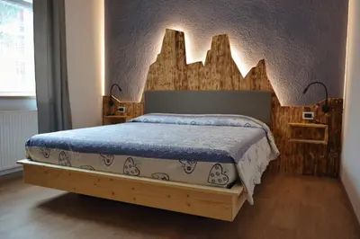 a bedroom with a bed with a wooden headboard at Hotel Nès Crépes in Pozza di Fassa