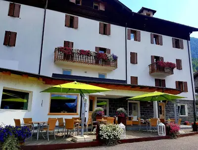 a hotel with tables and umbrellas in front of it at Ciasa Alpina Relax Hotel in Moena