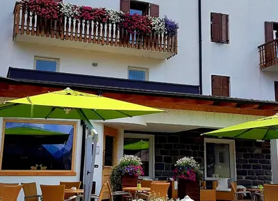 an outdoor cafe with tables and umbrellas in front of a building at Ciasa Alpina Relax Hotel in Moena