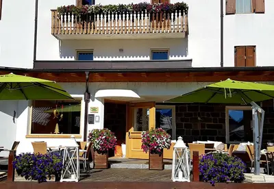 an outdoor cafe with tables and chairs and umbrellas at Ciasa Alpina Relax Hotel in Moena