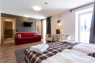 a bedroom with a large bed and a red couch at Ciasa Alpina Relax Hotel in Moena