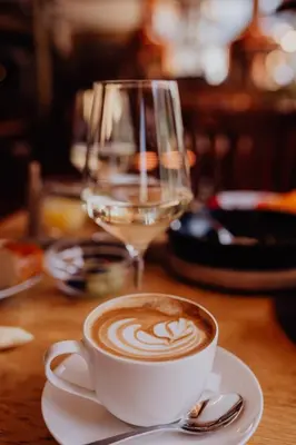 a cup of coffee on a table with a glass of wine at Martinerhof's Brauhotel in San Martino