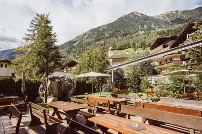 a patio with wooden tables and benches and a mountain at Martinerhof's Brauhotel in San Martino