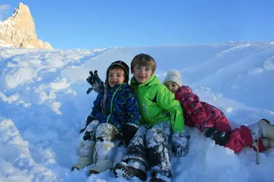 three young children sitting in the snow at Hotel Vienna in San Martino di Castrozza