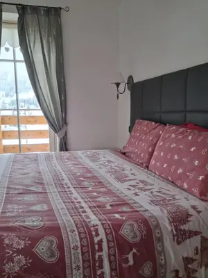 a bedroom with a bed with a red comforter and a window at Majon de la nona in Pozza di Fassa
