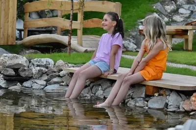 two little girls sitting on a bench by a pond at Ciasa Pedaga in San Vigilio Di Marebbe