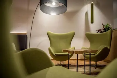 a waiting room with green chairs and a table at Hotel La Fradora - Dolomites Hotel in San Cassiano
