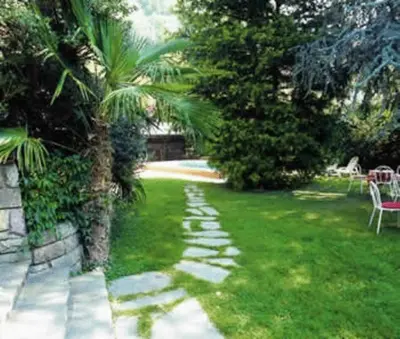 a garden with a palm tree and a stone path at Hotel Brunner in Merano