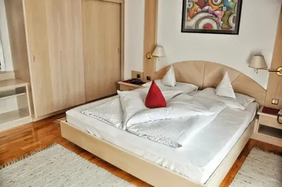 a large white bed with a red pillow on it at Hotel Brunner in Merano