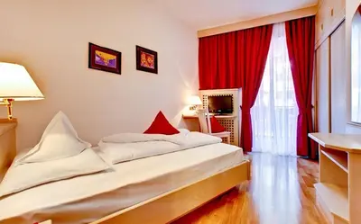 a bedroom with a large bed with red curtains at Hotel Brunner in Merano