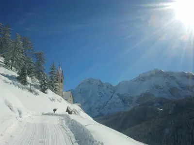 a snow covered road with a church in the mountains at Sumaela Apartments in La Valle