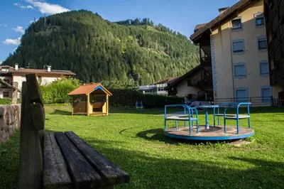 a park with a playground with a bench and a mountain at Aparthotel Majestic in Predazzo