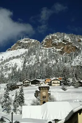a snow covered mountain with a village with a clock tower at Col Rodella in Campitello di Fassa