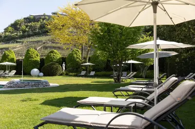 a row of lounge chairs with umbrellas in a park at Hotel Burggräflerhof in Merano