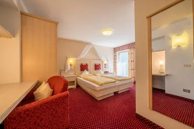 a bedroom with a bed and two chairs and a mirror at Hotel Dolomiti in La Villa