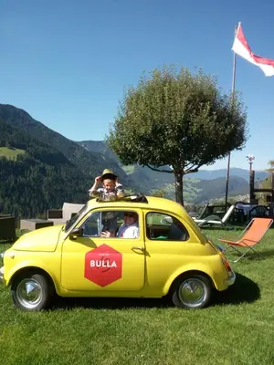a man sitting on top of a small yellow car at Albergo Somont in Ortisei