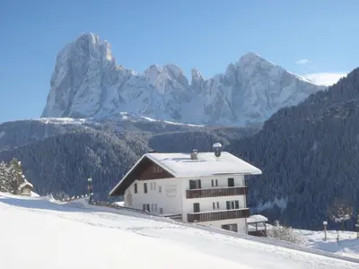 a building on a snowy hill with mountains in the background at Albergo Somont in Ortisei