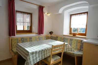 a small room with a table and a bench and windows at Soroea in San Vigilio Di Marebbe