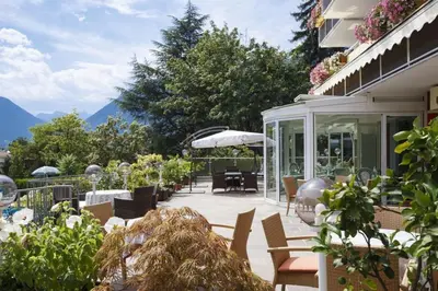 a patio with chairs and tables with mountains in the background at Hotel Tiffany in Merano