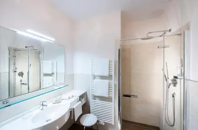 a white bathroom with a sink and a shower at Hotel Tiffany in Merano