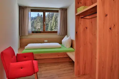 a room with a bed and a red chair at Familyparadies GAMPLALM in Lana