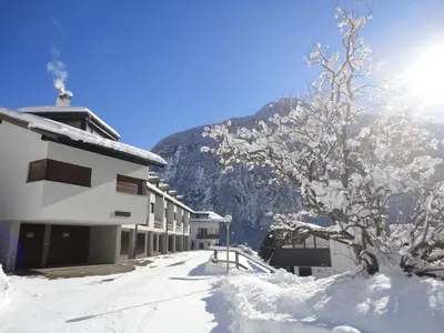 a snow covered tree next to a building with a mountain at Sella Ronda Apartment in Campitello di Fassa