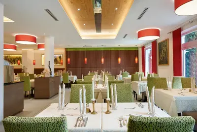 a dining room with white tables and green chairs at Hotel Anatol in Merano