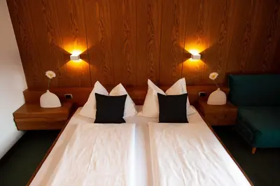 a bedroom with two beds and a green chair at Hotel Schönbrunn in Merano