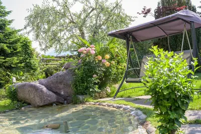 a small pond in a garden with a swing at Glanzhof Hotel & Apartments in Marlengo