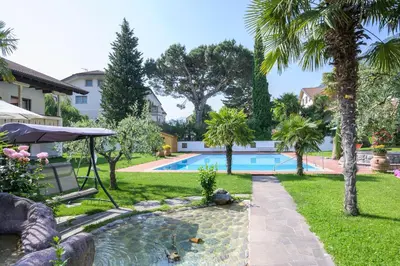 a backyard with a swimming pool and palm trees at Glanzhof Hotel & Apartments in Marlengo