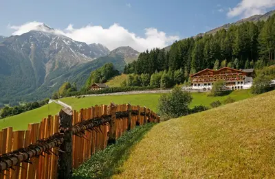 a wooden fence in a field with mountains in the background at Hotel Kranebitt in Val di Vizze