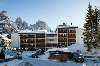 a snow covered building with cars parked in a parking lot at Residence Lastei in San Martino di Castrozza